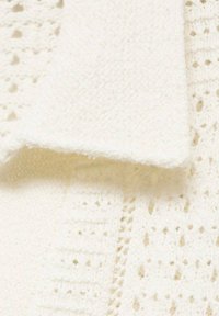 Tessuto bianco lavorato a maglia con una finitura testurizzata e motivi a traforo. Il design include filato morbido a boucle e un dettaglio di bordo liscio.