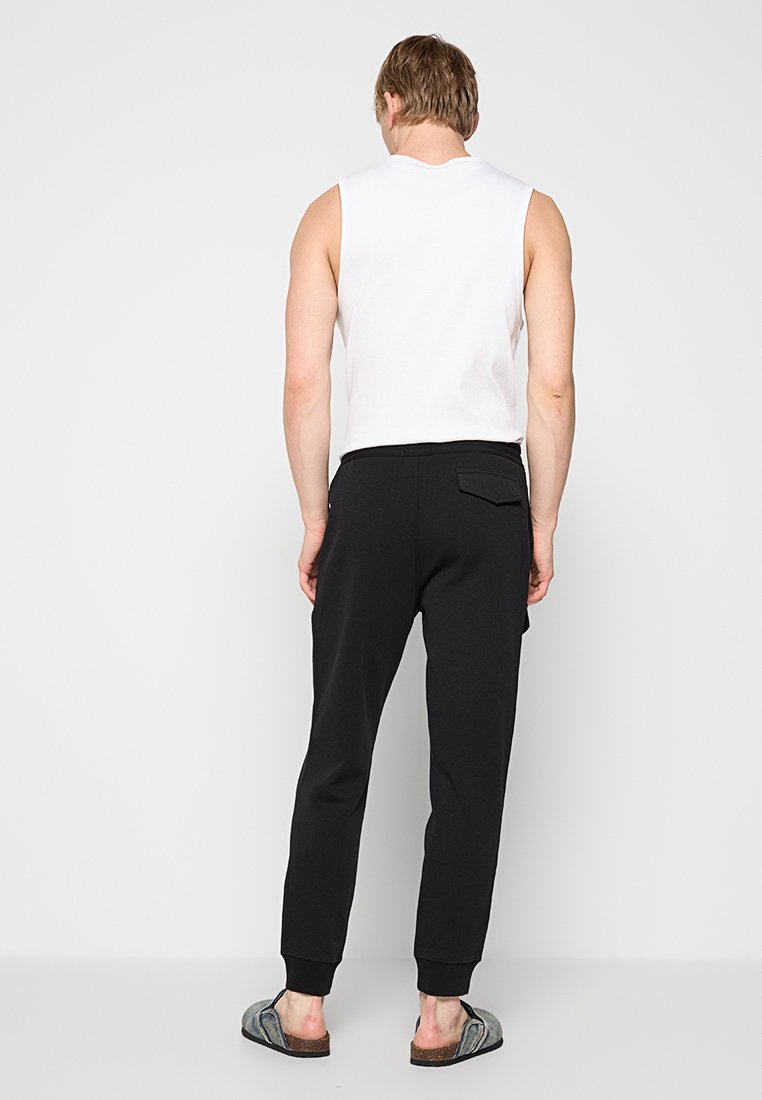 Biała top bez rękawów z okrągłym dekoltem, zestawiony z czarnymi spodniami dresowymi z ściągaczami przy kostkach i tylną kieszenią.