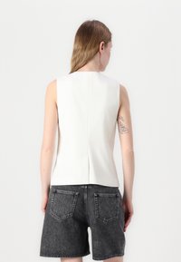 Hvit ermeløs topp med rette linjer og bakseam, sammen med høyt liv mørkegrå shorts med fem lommer.