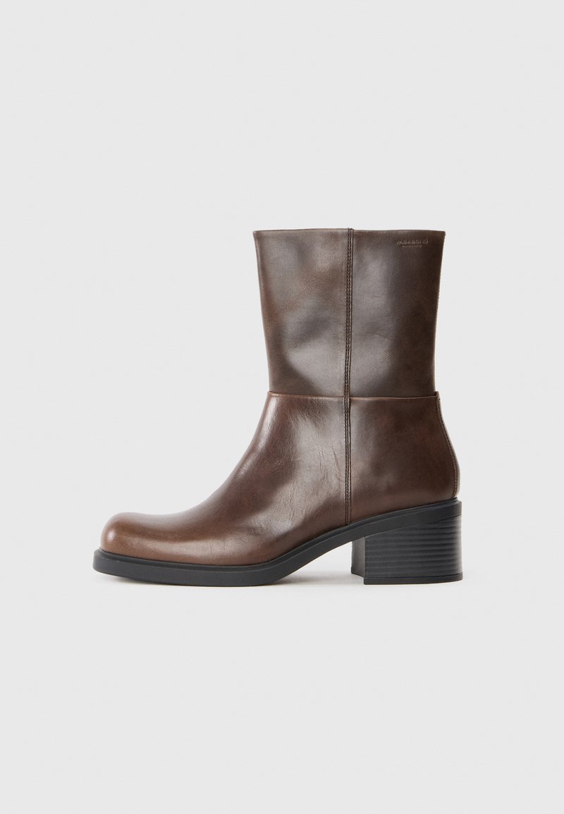 Brązowy skórzany botek na kostkę o gładkiej fakturze, zaokrąglonym nosku i słupkowym obcasie. Posiada minimalne przeszycia i oznaczenie marki z tyłu.