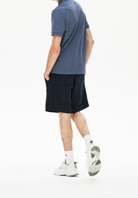 Námorníci modré polo tričko, černé pruhované šortky a bílé tenisky s šedými akcenty. Šortky mají boční kapsy a volný střih.