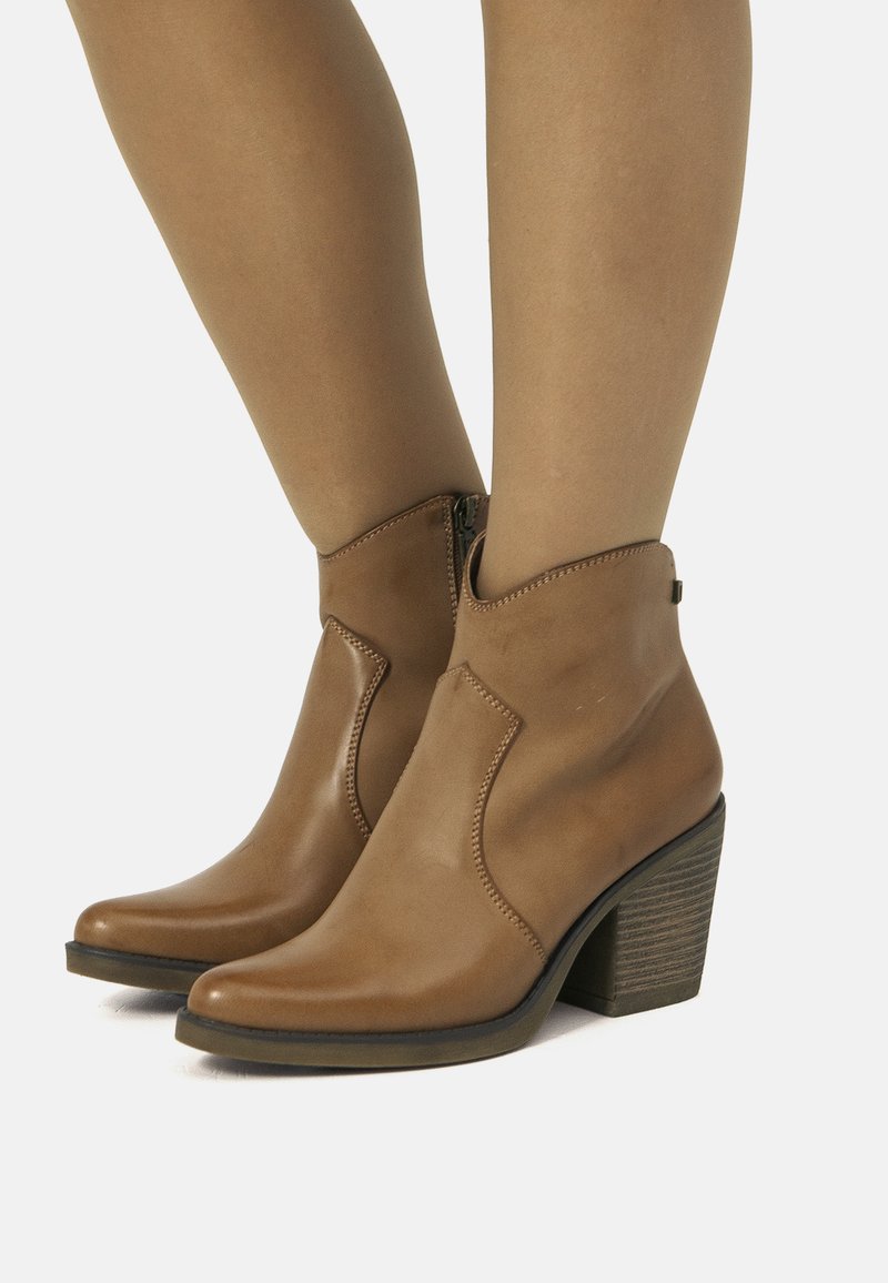 Botas de cuero marrón hasta el tobillo con puntera puntiaguda, detalles de costura y un tacón bajo en bloque. Cuentan con una cremallera lateral para facilitar su uso.