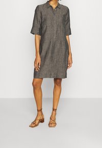Šedé lněné šaty košilového střihu s límečkem, krátkými rukávy a dvěma předními kapsami. Nosené s hnědými sandály na pásky s blokovým podpatkem.