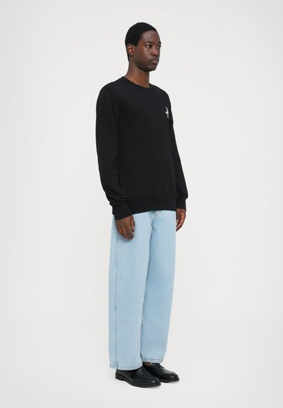 Black long-sleeve sweatshirt with a crew neckline, paired with light blue wide-leg jeans and black shoes, standing against a plain background.