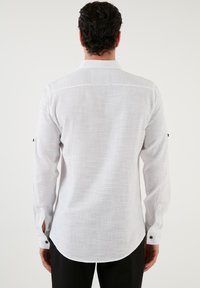 Witte blouse met lange mouwen, gemaakt van gestructureerde stof, met een gebogen zoom, knoopmanchetten, en kleine zwarte knoopaccenten op de mouwen.