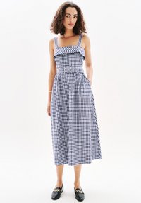 Sininen ja valkoinen ruudullinen midi-mekko, jossa on rypytetty yläosa, neliökaula-aukko, säädettävät olkaimet ja kapeutettu vyötärö. Yhdistetty mustiin loafer-kenkiin.