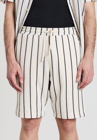 Shorts rayés blancs et bleu marine avec une taille élastique et un cordon de serrage. La texture est tissée, avec des rayures verticales contrastantes.