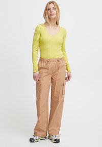 Langärmliges, geripptes, leuchtend gelbes Oberteil mit V-Ausschnitt. Beige Cargo-Hosen mit elastischem Bund, seitlichen Taschen und lockerer Passform.