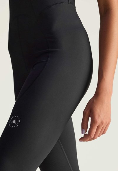 Black leggings made from stretchy material, featuring a sleek design, fitted shape, and a small white logo on the side.