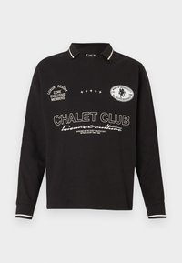 Polo a maniche lunghe nero con testo bianco "CHALET CLUB" e toppe, colletto e polsini a righe, stile casual.