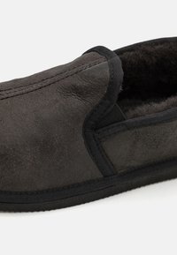 Mocassin en suede noir avec doublure intérieure douce, panneaux latéraux élastiques et semelle plate en caoutchouc. Présente une texture lisse et des coutures minimales.
