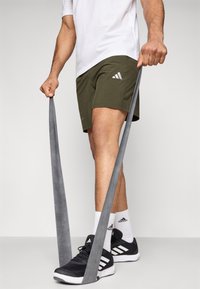 Zelene sportske kratke hlače s tri bijele pruge, crne tenisice, bijele čarape i sivi otporni trak, s naglaskom na funkcionalnost i dizajn.