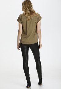 Camiseta de manga corta verde oliva combinada con pantalones de cuero negro ajustados, que presentan una textura suave y un diseño elegante.