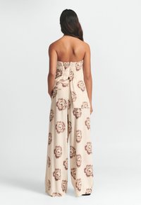 Strapless beige topp med en gathered back, paras med vida byxor som har ett brunt blommönster genom hela. Slät, lättviktig tyg.