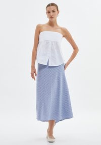 Ärmelloses weißes Oberteil mit strukturiertem Oberteil und Knopfleiste, kombiniert mit einem blau-weißen gestreiften Maxikleid mit einem fließenden Saum.