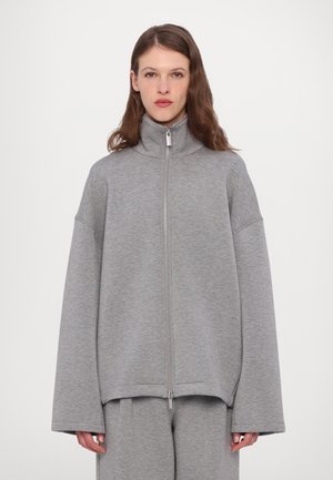 Harmaa vetoketjullinen fleece-takki, jossa on korkea kaulus, leveät hihat ja sileä pinta. Varustettu metallivetoketjulla ja yhteensopivilla harmailla housuilla.