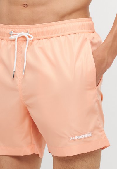Ferskenfargede svømmedraktshorts med glatt, lett stoff, elastisk midje, hvit snor, sidelommer og en liten logo på bunnen.