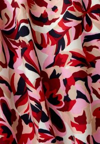 Blumenerstoff mit einer Mischung aus roten, rosa und schwarzen Mustern auf einem cremigen Hintergrund, mit weicher Textur und fließendem Design.