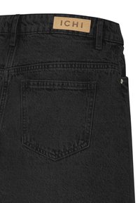 Jean en denim noir avec un patch en cuir portant l'inscription "ICHI" au niveau de la taille, une poche arrière unique et une finition texturée.