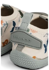 Világos bézs színű szövetcipők színes virágmintával, szürke díszítésekkel és texturált gumitalppal, amelyen húzófül is található a könnyű felvételhez.