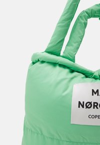 Borsa a tracolla imbottita verde con manici spessi e intrecciati, dotata di etichetta bianca con testo nero e una texture liscia e morbida.