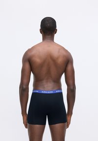 Rear view of a shirtless man wearing black Björn Borg boxer briefs with a blue waistband against a plain light background.