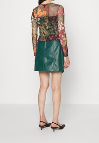 Blommönstrad, transparent långärmad topp lager på en figurnära, grön läder minikjol med rak nederkant och dragkedja bak. Svarta klacksko.