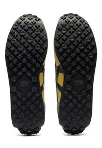 Suole delle scarpe in gomma nera con un motivo di trazione multi direzionale, con accenti gialli e grigi. Include impugnature modellate a forma di fiore.