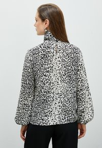 Svart och vit leopardmönstrad blus med hög krage, långa puffärmar och en liten nyckelhålsdetalj bak, tillverkad av lätt tyg.