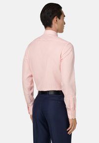 Jasnoróżowa koszula z długim rękawem z teksturowanym wzorem, z zapięciem na guziki przy mankietach i klasycznym kołnierzykiem, w zestawie z ciemnoniebieskimi spodniami typu tailor.