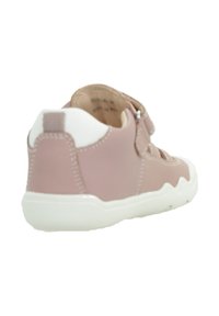 Zapatilla sintética rosa con suela de goma blanca, con textura suave, forma redondeada y cierre de tira ampliable.