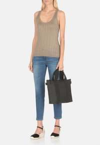 Borsa a spalla nera con doppi manici, realizzata in materiale morbido, con una forma rettangolare e dettagli di texture a contrasto. Abbinata a jeans azzurri e un top a righe beige.