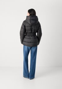 Zwarte pufferjack met een verbonden capuchon, smal getailleerde taille en geribde riem. De stof heeft een gewatteerde textuur met horizontale panelen.