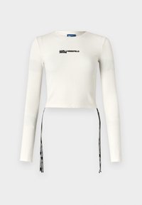 Bijela dugih rukava skraćena majica s rebrastom teksturom, s crnim logotipom "KARL LAGERFELD JEANS" i podesivim vezicama na rubu.