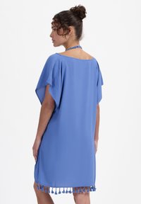 Modrý kaftan vyrobený z lehkého materiálu s volným střihem, s krátkými rukávy a lemem zdobeným třásněmi.