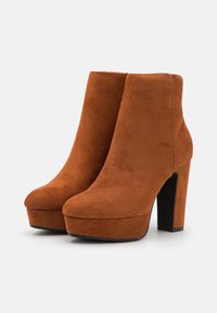 Bottes chelsea en daim marron, avec un talon bloc haut et une semelle plateforme. Texture lisse et design minimaliste, sans matériel ni accents visibles.