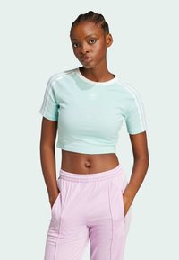 Ljust teal kortärmad t-shirt med vita detaljer och tre ränder på ärmarna, tillsammans med rosa byxor med fickor.