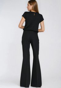 Czarna bluzka z krótkimi rękawami i wycięciem na plecach, zestawiona z czarnymi, rozszerzanymi spodniami z wysokim stanem, gładka faktura, dopasowany krój.