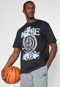 Μαύρο κοντομάνικο μπλουζάκι με γραφική εκτύπωση ενός καλαθοσφαιριστή και κείμενο "NIKE HOOPS". Κατασκευασμένο από βαμβακερό υλικό, σε χαλαρή εφαρμογή.