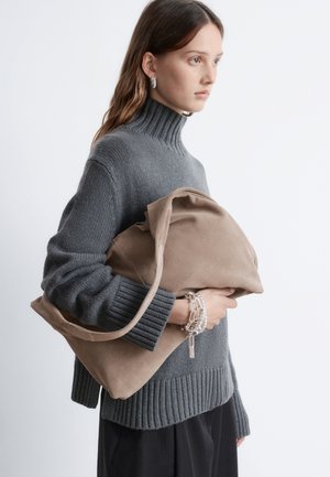 Gray knit sweater with ribbed collar, holding a brown suede bag. Notable details include layered bracelets and a relaxed bag shape.