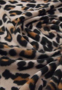 Tissu doux avec un motif léopard noir et brun sur un fond beige clair, présenté en plis délicats.