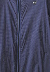 Námořnická modrá lehká bunda s texturovanou tkaninou, plným předním zipem a malým logem na levém horním rohu.