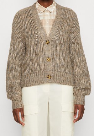 Cárdigan beige de punto grueso con tres botones de carey sobre una camisa de cuadros beige con cuello, combinado con pantalones cargo crema.