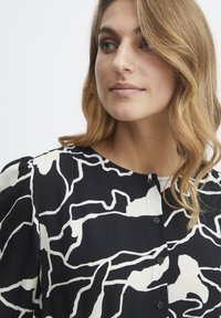 Blusa de patrón en blanco y negro con líneas abstractas, escote redondo, cierre frontal de botones y textura de tela suave.