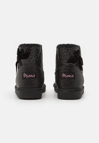 Botas negras hasta el tobillo de material brillante, con un acento de lazo y un logo rosa, panel trasero texturizado y suela de goma negra.