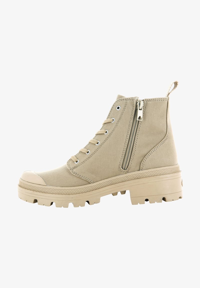 Bottine en toile beige avec un embout en caoutchouc, un laçage à l'avant, une fermeture éclair sur le côté et une semelle texturée antidérapante. Elle présente des œillets et une languette.