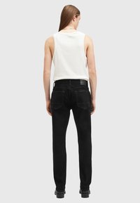 Los jeans de mezclilla negros tienen un corte ajustado con bolsillos traseros y una tela texturizada. Se combinan con una blusa sin mangas blanca y botas negras.