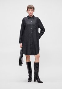 Σκούρο τζιν φόρεμα με κουμπιά μπροστά, μακριά μανίκια και πλαϊκή τσέπη. Φορεμένο με μαύρες μπότες μέχρι το γόνατο και μαύρη τσάντα.