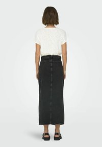 Zwart denim maxi-rok met een aansluitende taille en een rafelige zoom, gecombineerd met een lichtgekleurde top met korte mouwen. Platte sandalen maken de look compleet.