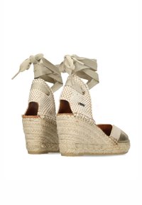 Zeppe espadrille beige con tomaia intrecciata, suola in juta spessa e lacci alla caviglia. La punta ha un accento metallico con una finitura testurizzata.
